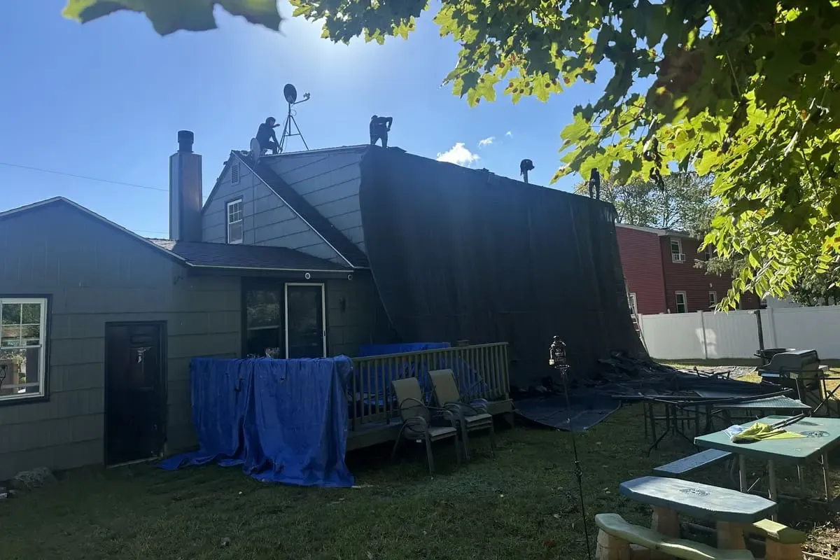Prescott Roofing crew on roof with protective tarps covering landscaping during emergency repair